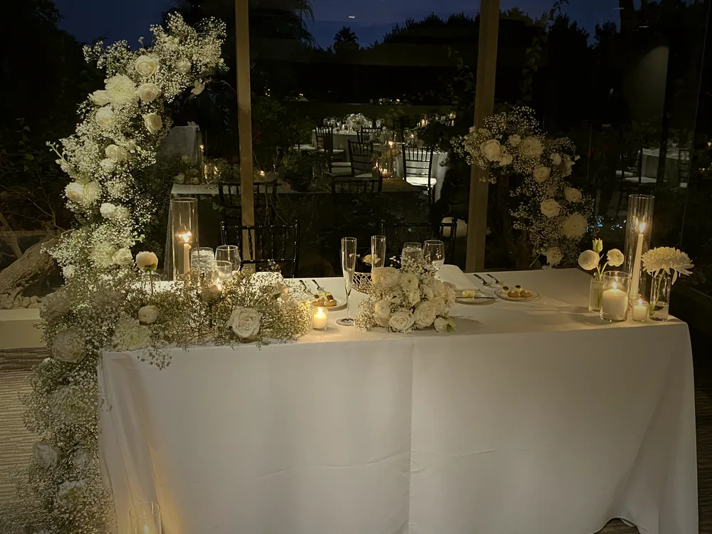 Sweetheart table under a white floral arch at dusk